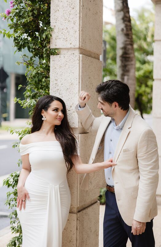 Iviani reaching for Joey’s hand beside a vine-covered column