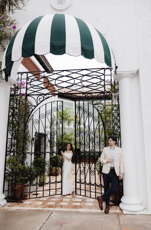 Iviani and Joey beneath a green-striped awning at an iron gate