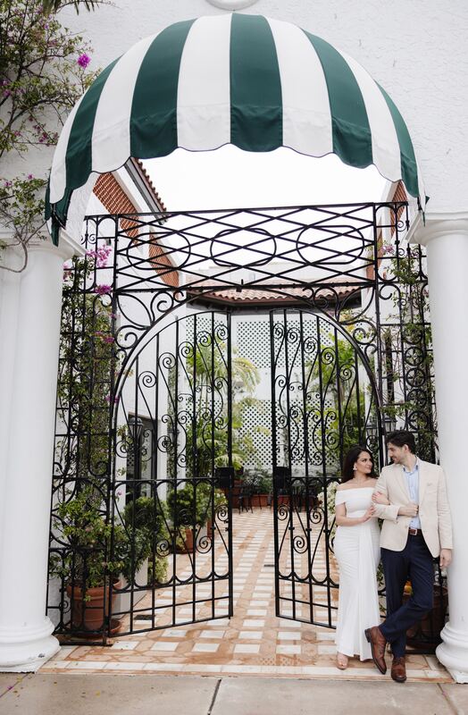 Iviani and Joey framed by a wrought-iron gate under a striped awning